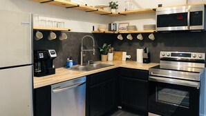 Una cocina moderna con electrodomésticos de acero inoxidable, estantes de madera y un protector contra salpicaduras negro.