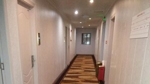 Un couloir d’hôtel avec un tapis à motifs, des portes et un extincteur.
