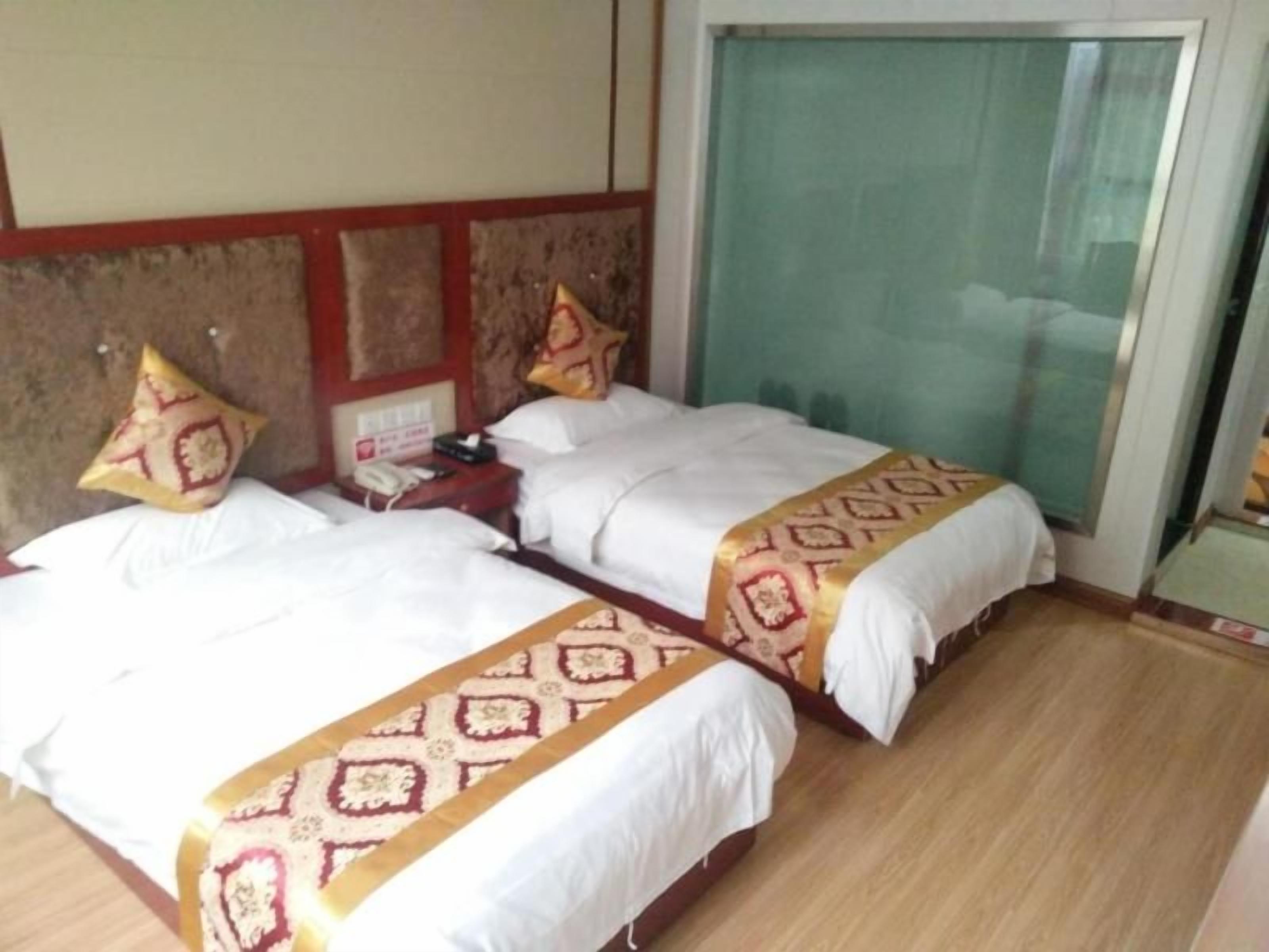 A hotel room with two beds, each with a patterned bedspread and pillows. There is a bedside table with a lamp and a telephone.
