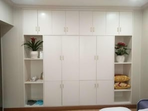 Un armario blanco con varias puertas y estantes, algunos con objetos como zapatos y plantas.