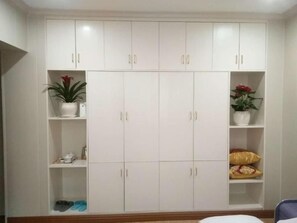 A white wardrobe with multiple doors and shelves, some with items like shoes and plants.