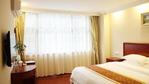 Une chambre d’hôtel comprenant un lit, une table de chevet, une lampe, une fenêtre avec des rideaux et un climatiseur fixé au mur.