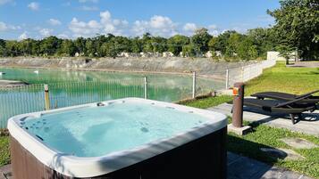 Un jacuzzi con revestimiento de madera, rodeado por un área de césped y una valla.