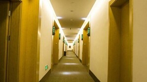 Pasillo de hotel con puertas a ambos lados, señales de salida de emergencia y suelo alfombrado.