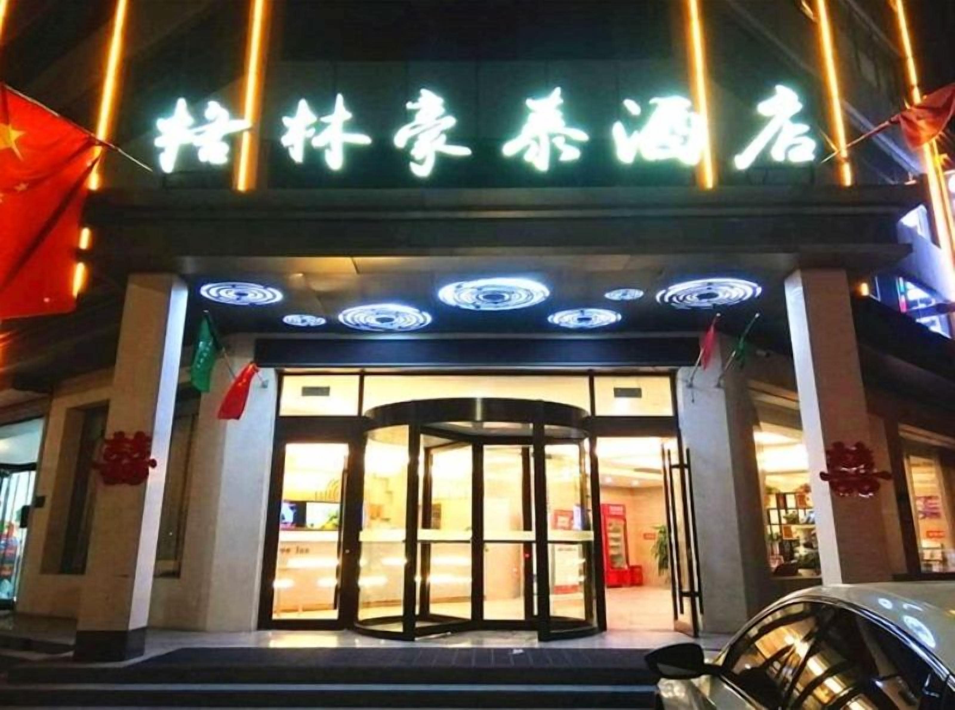 Entrada de hotel com porta giratória e letreiros iluminados.