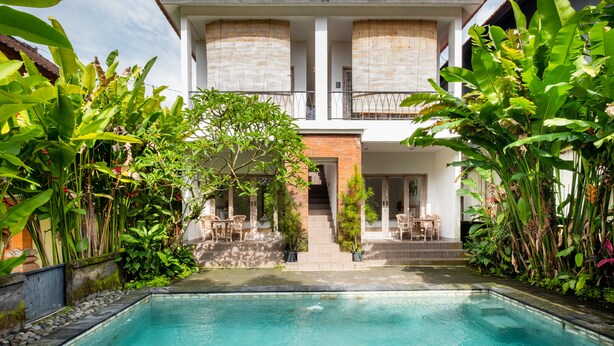A two-story house with a swimming pool, surrounded by lush greenery and a traditional tiled roof. - Suweta Homestay by Supala (Ubud)