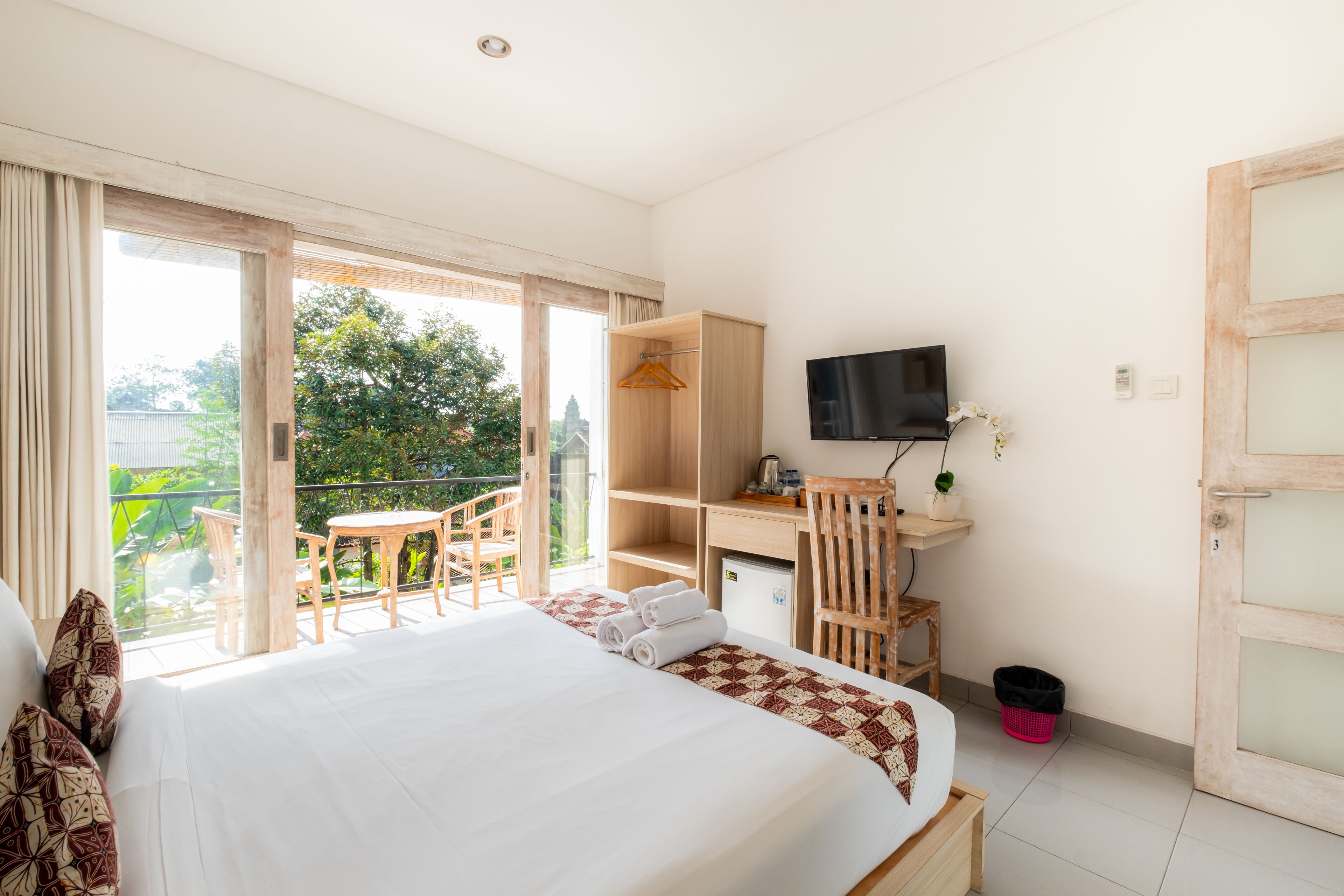 A hotel room with a bed, a desk, a TV, and a balcony with a table and chairs.