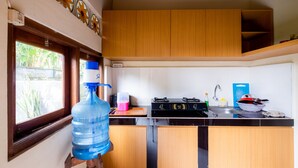 A kitchen with wooden cabinets, a stove, a sink, and a large water dispenser. - Suweta Homestay by Supala (Ubud)