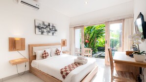 A modern hotel room with a large bed, a desk, and a view of lush greenery outside. - Suweta Homestay by Supala (Ubud)