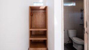 A bathroom with a toilet, a shower, and a wooden shelf unit. - Suweta Homestay by Supala (Ubud)