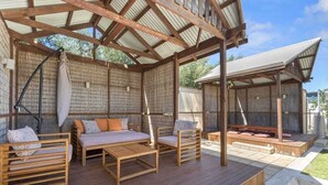 Eine Terrasse im Freien mit Holzmöbeln, einer überdachten Sitzgelegenheit und einer Ziegelwand.
