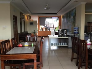 A spacious dining area with a long wooden table and chairs, a kitchen area with appliances, and a staircase leading to an outdoor area. - Belitong Inn Hotel Belitung (Tanjung Pandan)