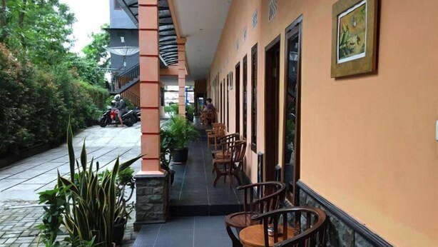A covered outdoor seating area with wooden chairs and tables, potted plants, and a tiled floor. - Belitong Inn Hotel Belitung (Tanjung Pandan)
