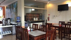 A restaurant with wooden tables and chairs, a coffee station, and a television mounted on the wall. - Belitong Inn Hotel Belitung (Tanjung Pandan)