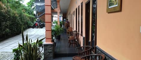 A corridor with chairs and tables, potted plants, and a motorcycle parked outside.