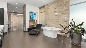 Ein modernes Badezimmer mit einer freistehenden Badewanne, einem Lounge-Sessel und einer großen Topfpflanze.