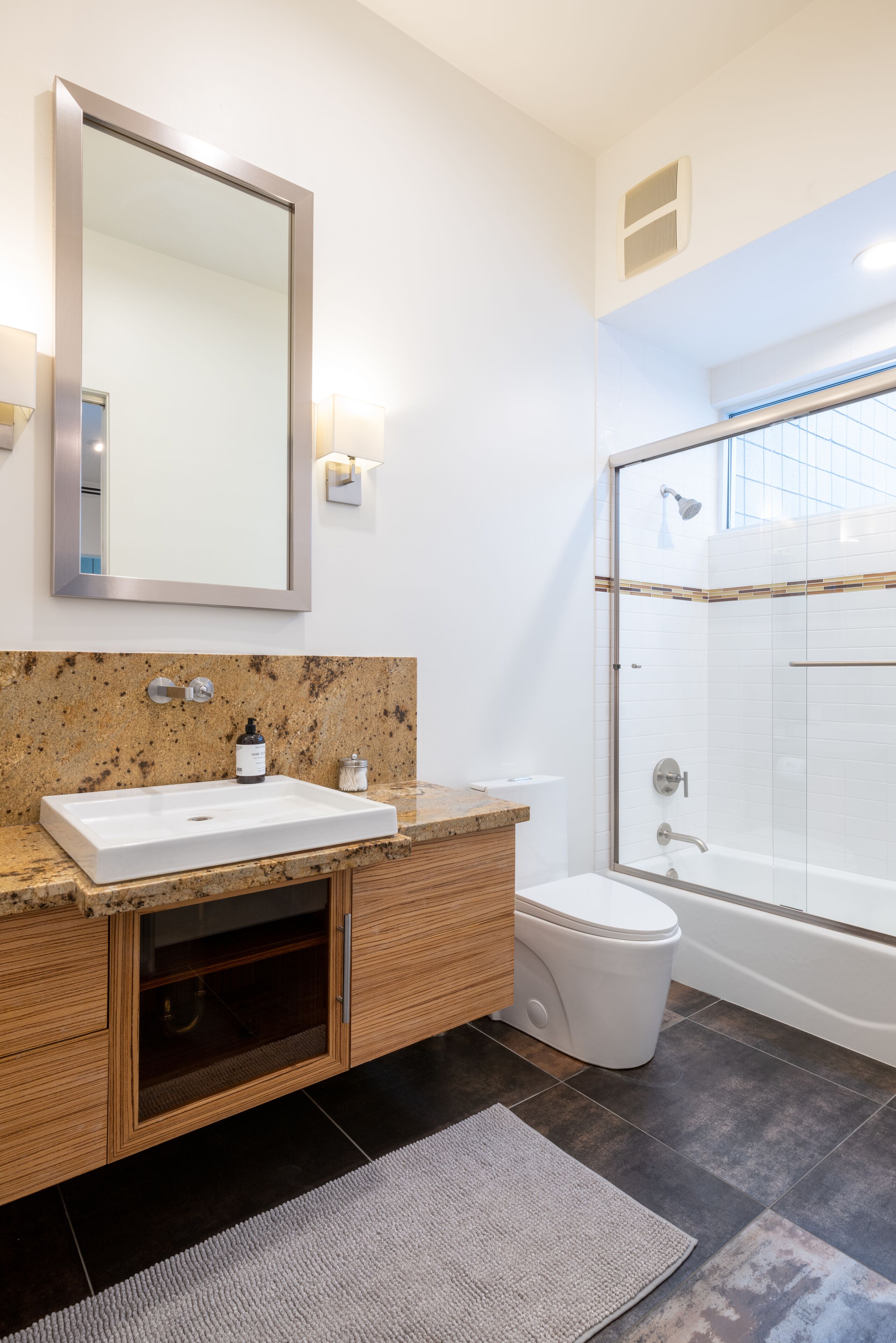 A modern bathroom with a large mirror, granite countertop, wooden vanity, white sink, toilet, and a glass-enclosed shower.