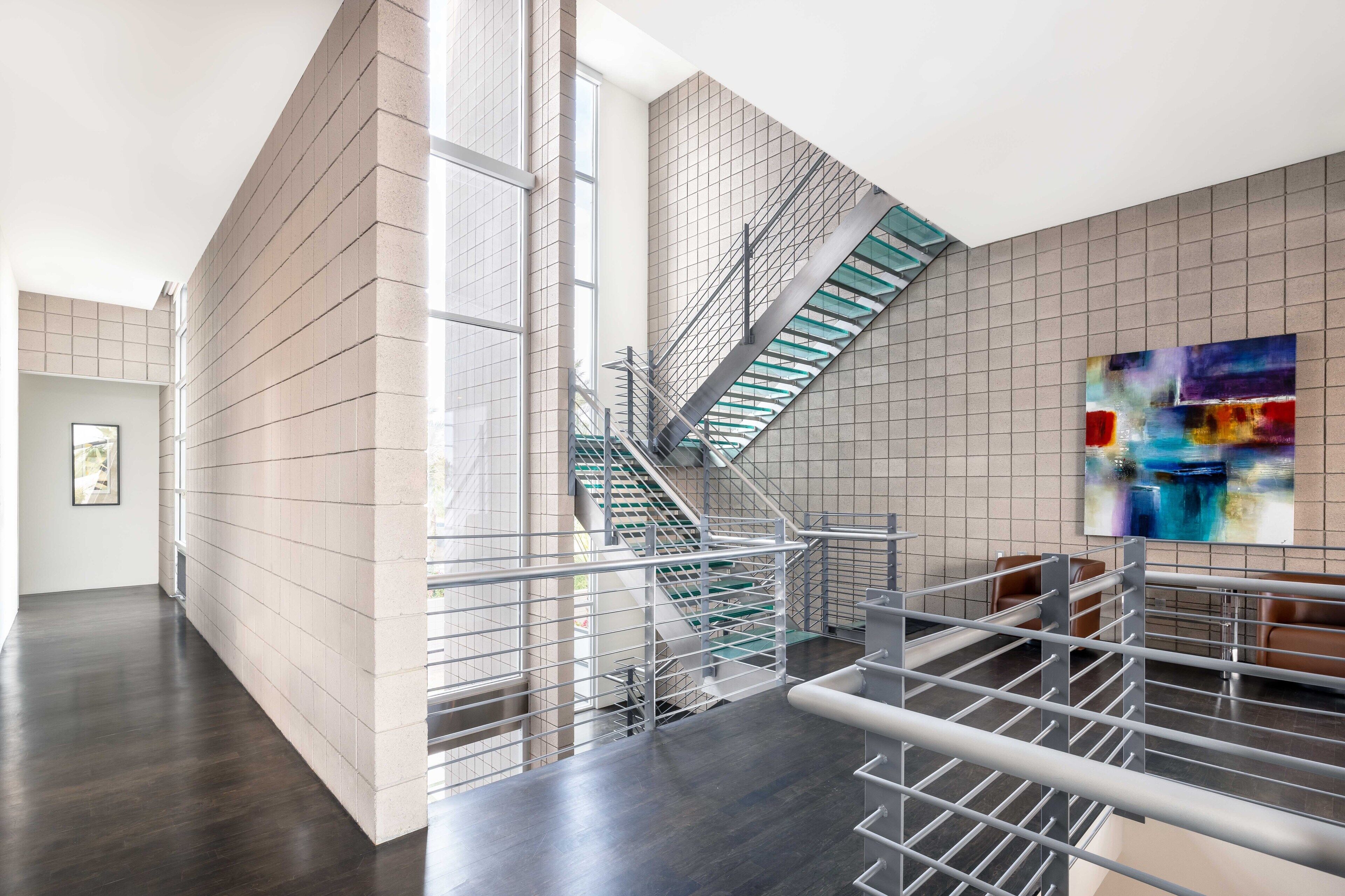 Un intérieur moderne avec un escalier, des rampes en métal et un tableau abstrait contemporain.
