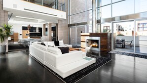 Ein großzügiger Wohnbereich mit einem weißen Sofa, einem Kamin und großen Fenstern mit Blick ins Freie.