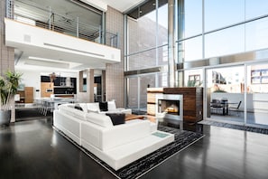 Relax in a spacious room with a central seating area, kitchen, and dining space, featuring a fireplace and large windows.