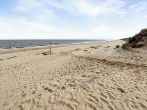A sandy beach with footprints, a metal sign, and a grassy cliff.
