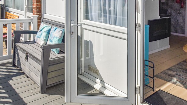 Een houten terras met een bank, een schuifdeur en een televisie op de achtergrond.