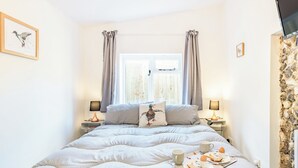 A bedroom with a large bed, two bedside tables with lamps, a window with curtains, and a stone wall.