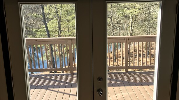 A wooden deck with a railing, leading to a door with a view of a forested area. - Lake House w/ Pool and King Bed, Fishing - Dogs OK (Hedgesville)