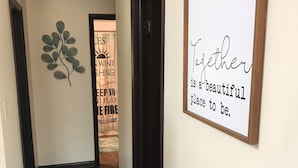 A hallway with a wooden floor, a wall-mounted sign with the text "Together is a beautiful place to be.", and a decorative metal leaf on the wall. - Lake House w/ Pool and King Bed, Fishing - Dogs OK (Hedgesville)