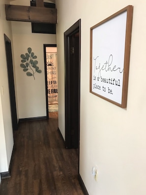 Un pasillo con suelo de madera, un letrero en la pared con el texto "Together is a beautiful place to be." y una hoja de metal decorativa en la pared.