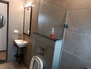 Un bany modern amb una cabina de dutxa de vidre, un lavabo blanc i un vàter.