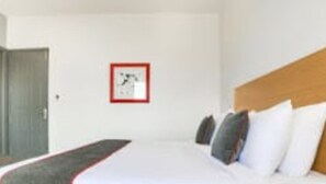 Una habitació d'hotel amb un llit, un panell de capçalera de fusta i un quadre a la paret.