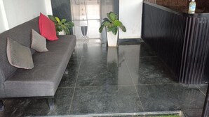 A reception area with a grey sofa, two potted plants, and a reception desk. - DBR Suites, Sarjapur Road (Bengaluru)