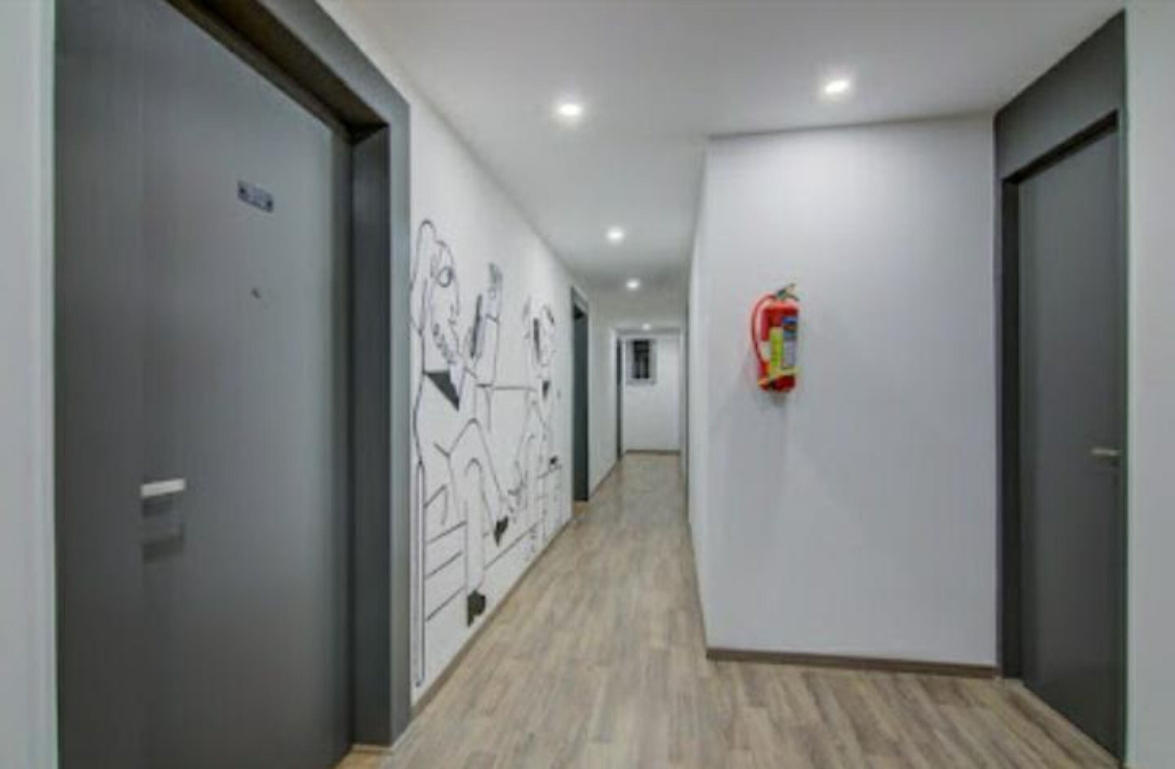 A corridor with grey doors, a fire extinguisher mounted on the wall, and a wooden floor.