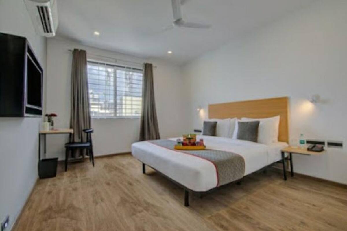 A hotel room with a bed, a desk, a chair, a TV, and a window with curtains.