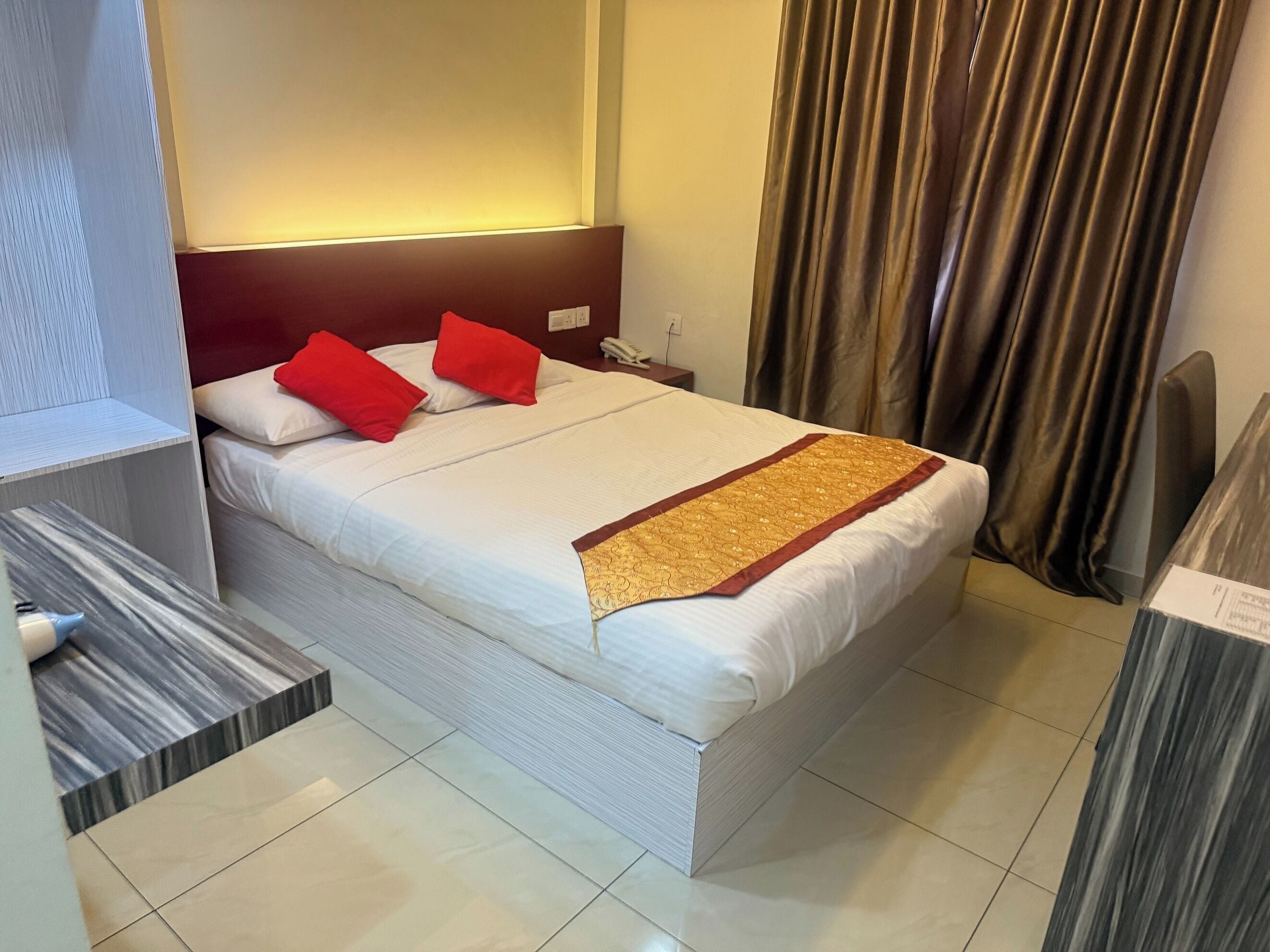 A neatly made bed with white linens, red pillows, and a decorative gold runner.