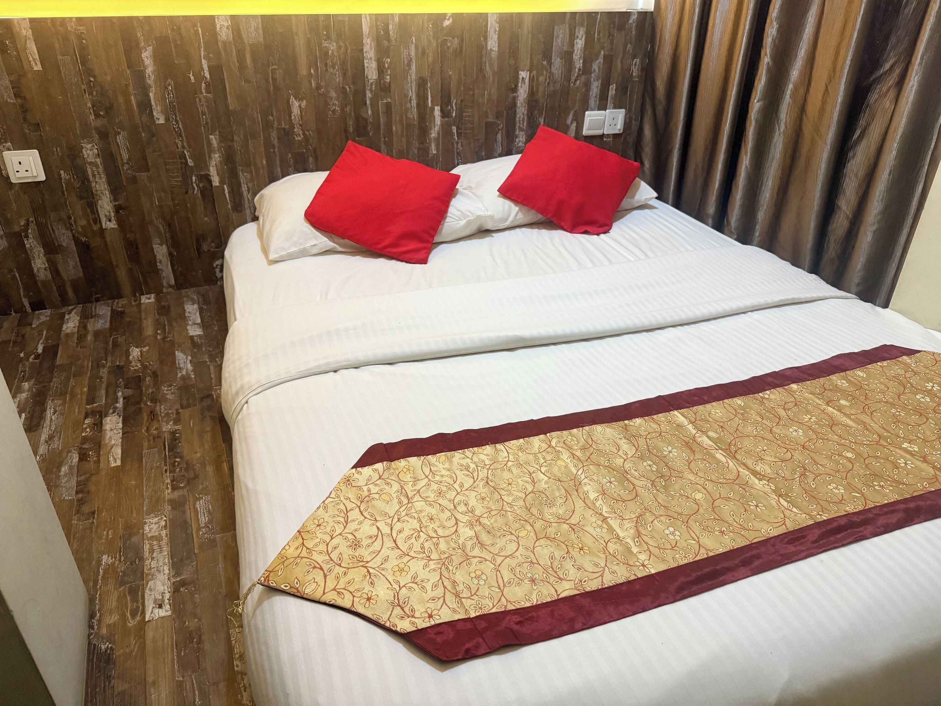 A neatly made bed with white bedding and a decorative red and gold throw blanket.