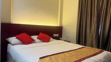 Une chambre d’hôtel avec un lit, des oreillers rouges, un couvre-lit blanc et un chemin de table décoratif aux motifs dorés et rouges.