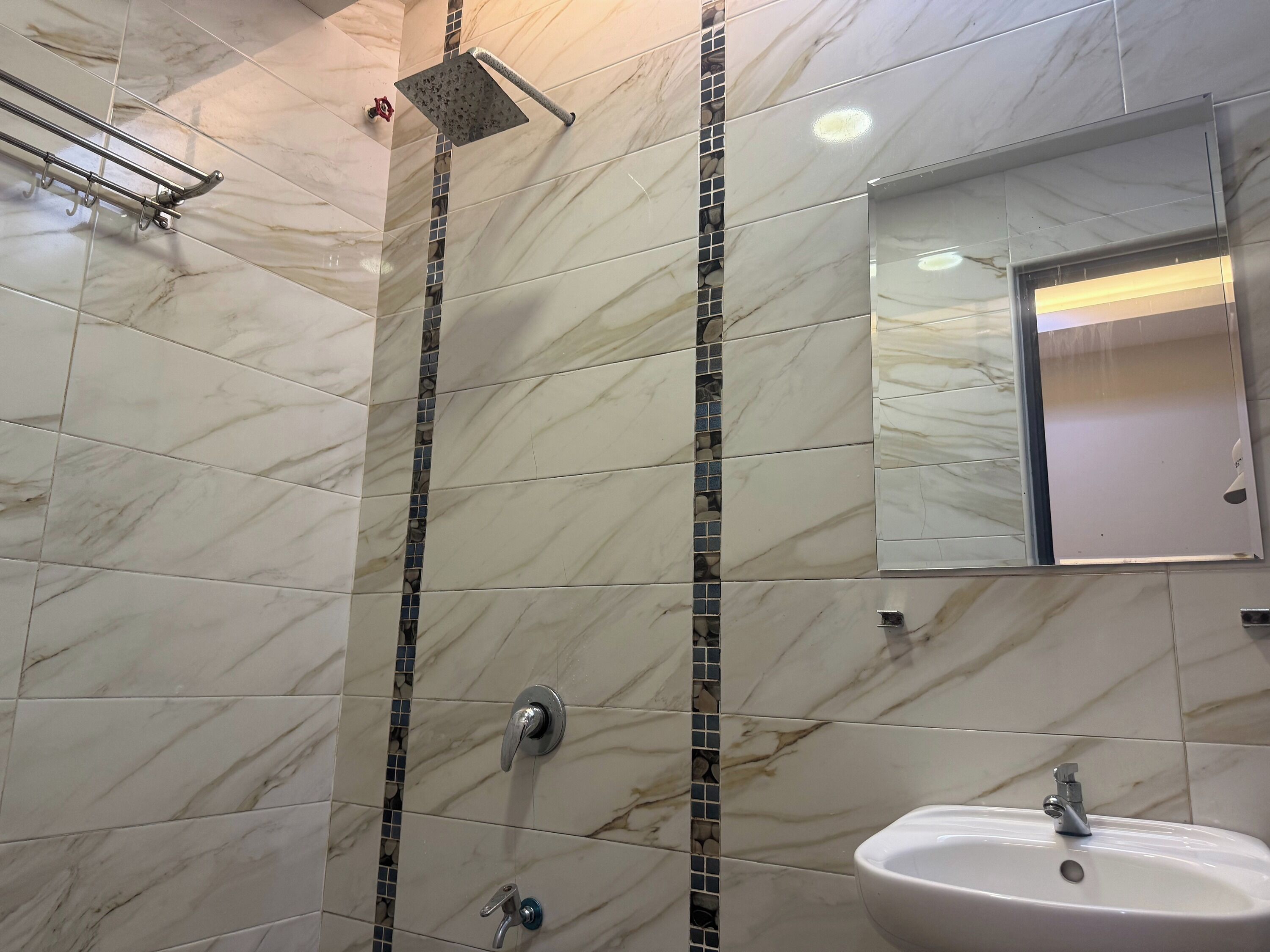A bathroom with a sink, mirror, shower, and tiled walls.