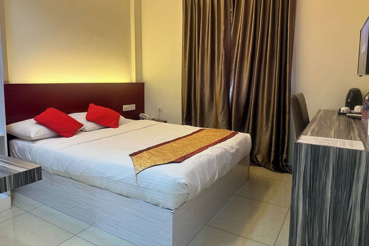 A hotel room with a large bed, a desk, and a curtain.