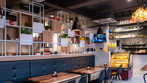 A modern restaurant with wooden tables, black cushioned booths, and a counter with a display case. - Hope Hotel Masai (Masai)