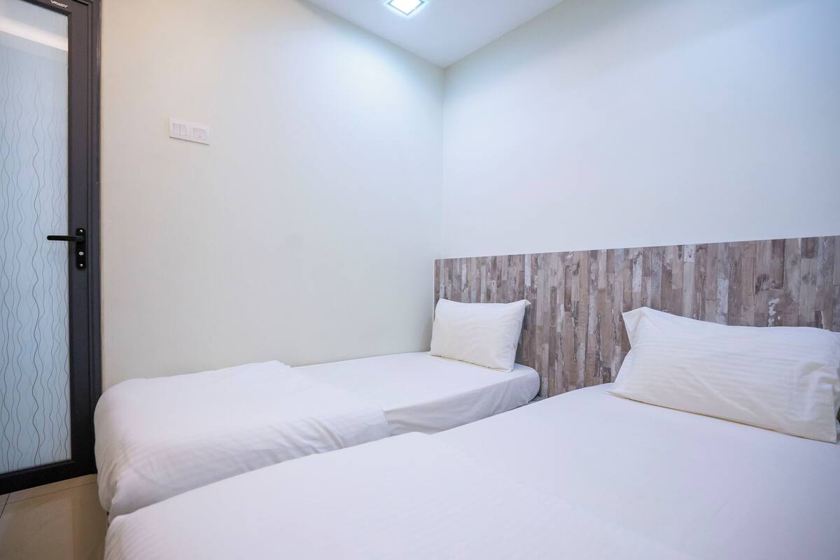 A room with two beds, a wooden headboard, a door with a glass panel, and a light switch on the wall.