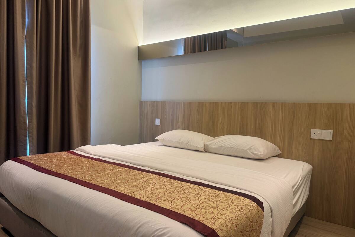 A hotel room with a large bed, a wooden headboard, and a window with curtains.