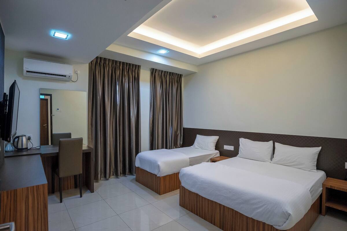 A hotel room with two beds, a desk, a chair, and a television.