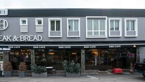 A building with multiple B&B cafes, each with a glass front and outdoor seating area. - Hope Hotel Masai (Masai)