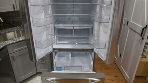 Ein offener Kühlschrank mit mehreren durchsichtigen Ablagen und einem Gefrierfach unten.