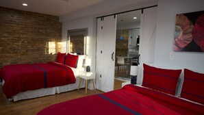 Ein Schlafzimmer mit zwei Betten, einem weißen Schreibtisch und einer Schiebetür zu einem Küchenbereich.