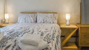 Un lit bien fait, avec une literie à motifs floraux, deux lampes de chevet et une table de chevet en bois.