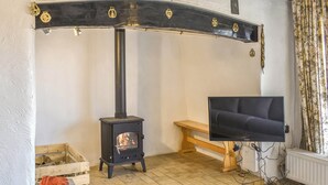Un salon chaleureux avec un poêle à bois, une télévision et un banc.
