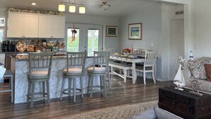 Una cocina amplia con una isla central, un comedor con una mesa y sillas blancas, y un ventilador de techo.